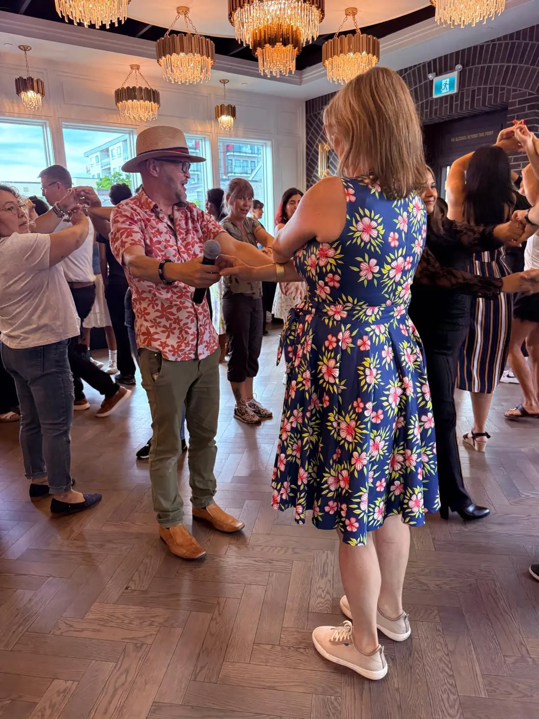 Salsa Paul with a microphone, leading a partner through a move in front of the class