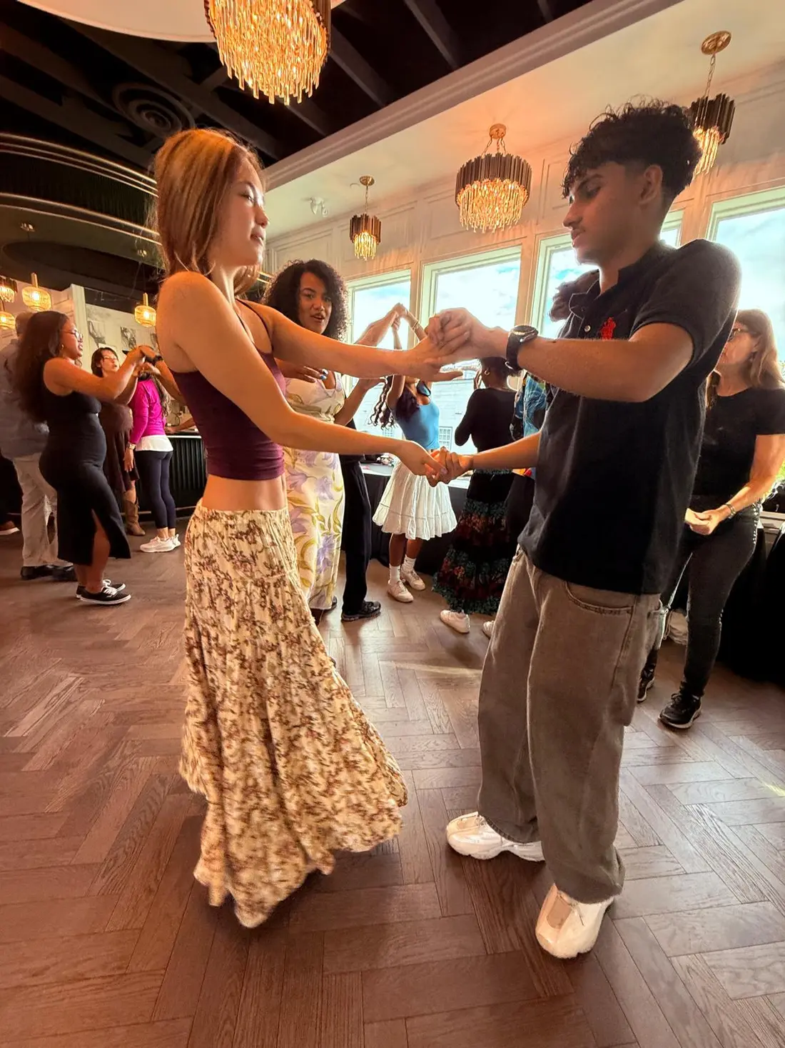 A dancer leading a partner through a turn in a busy room