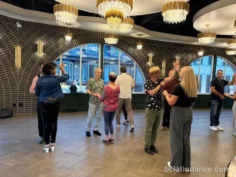 The class spread across the floor in partner hold beneath the chandeliers at Tuesday Salsa Nights, The Grand Hall, Chilliwack